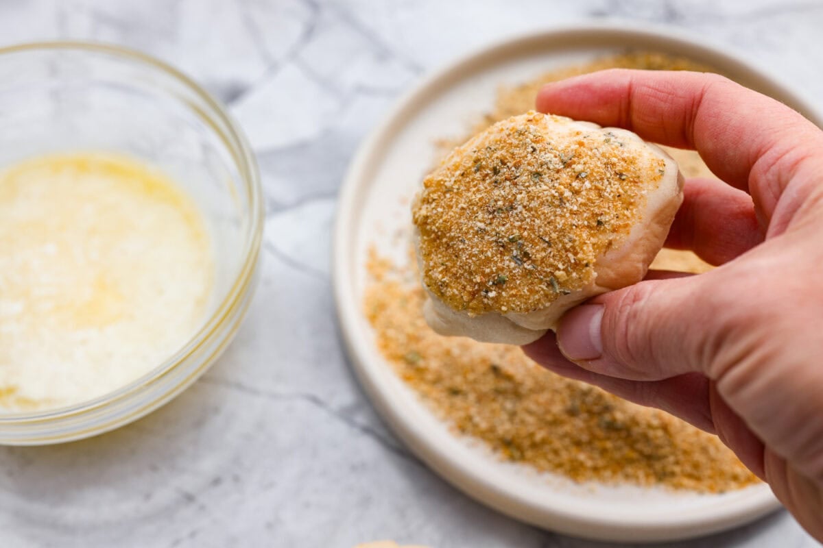 Someone coating the chicken pillows with butter and seasoned breadcrumbs. 