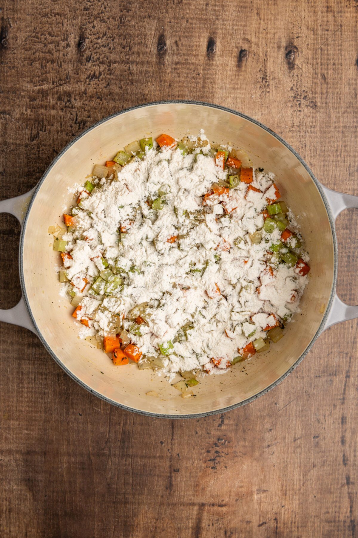 Dutch oven with flour sprinkled onto cooked vegetable mixture.