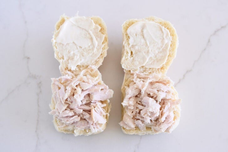 Two rolls open, spread with mayo, and shredded turkey on bottom half.