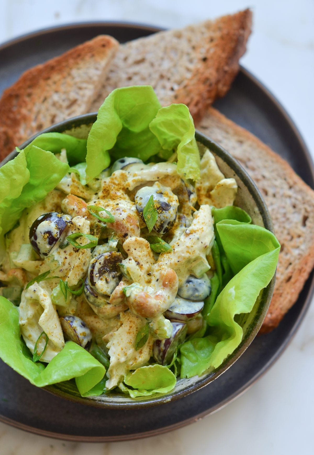 Chicken salad with grapes and almonds over lettuce in a bowl.