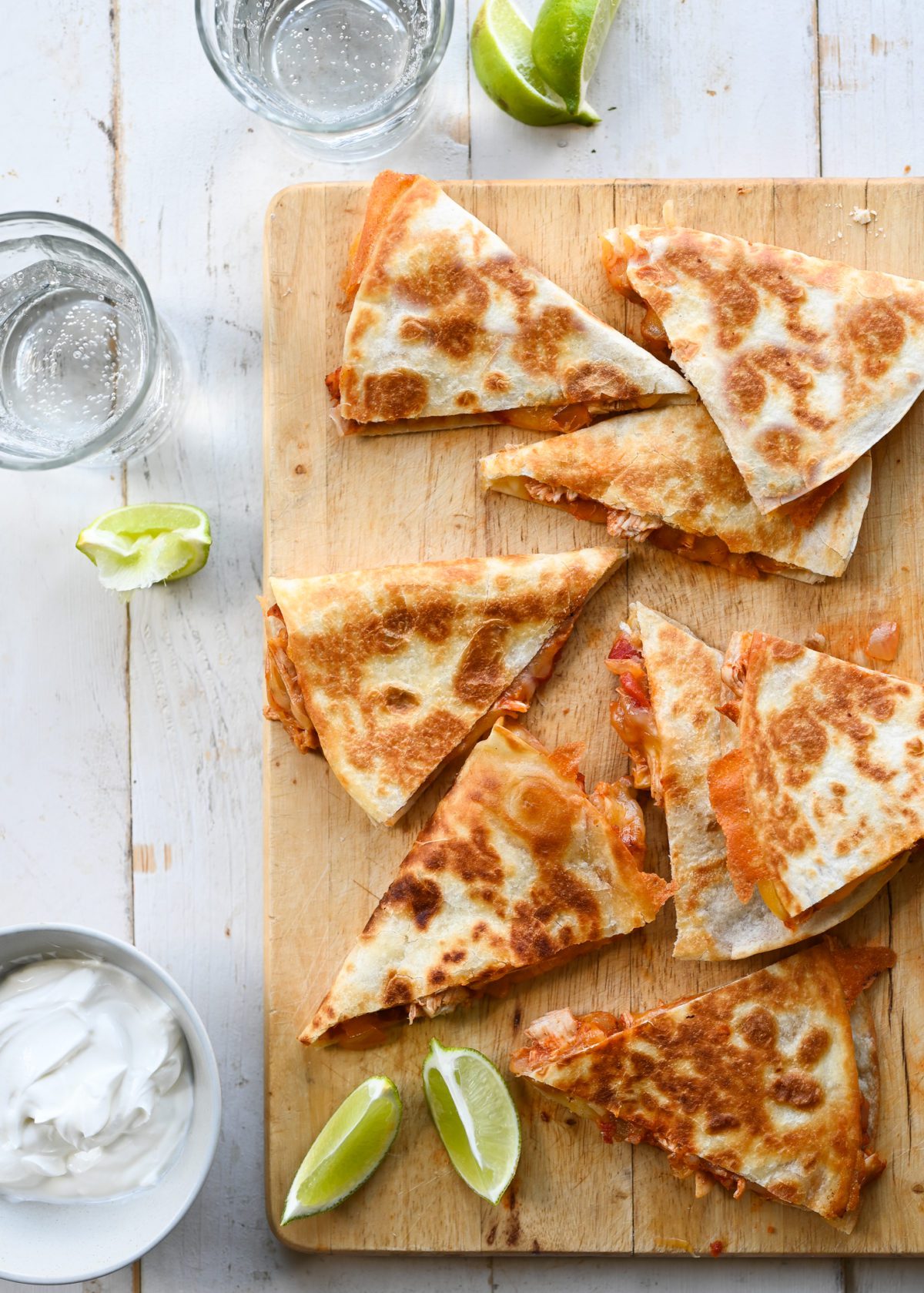 chicken quesadillas on wooden cutting board with limes and sour cream