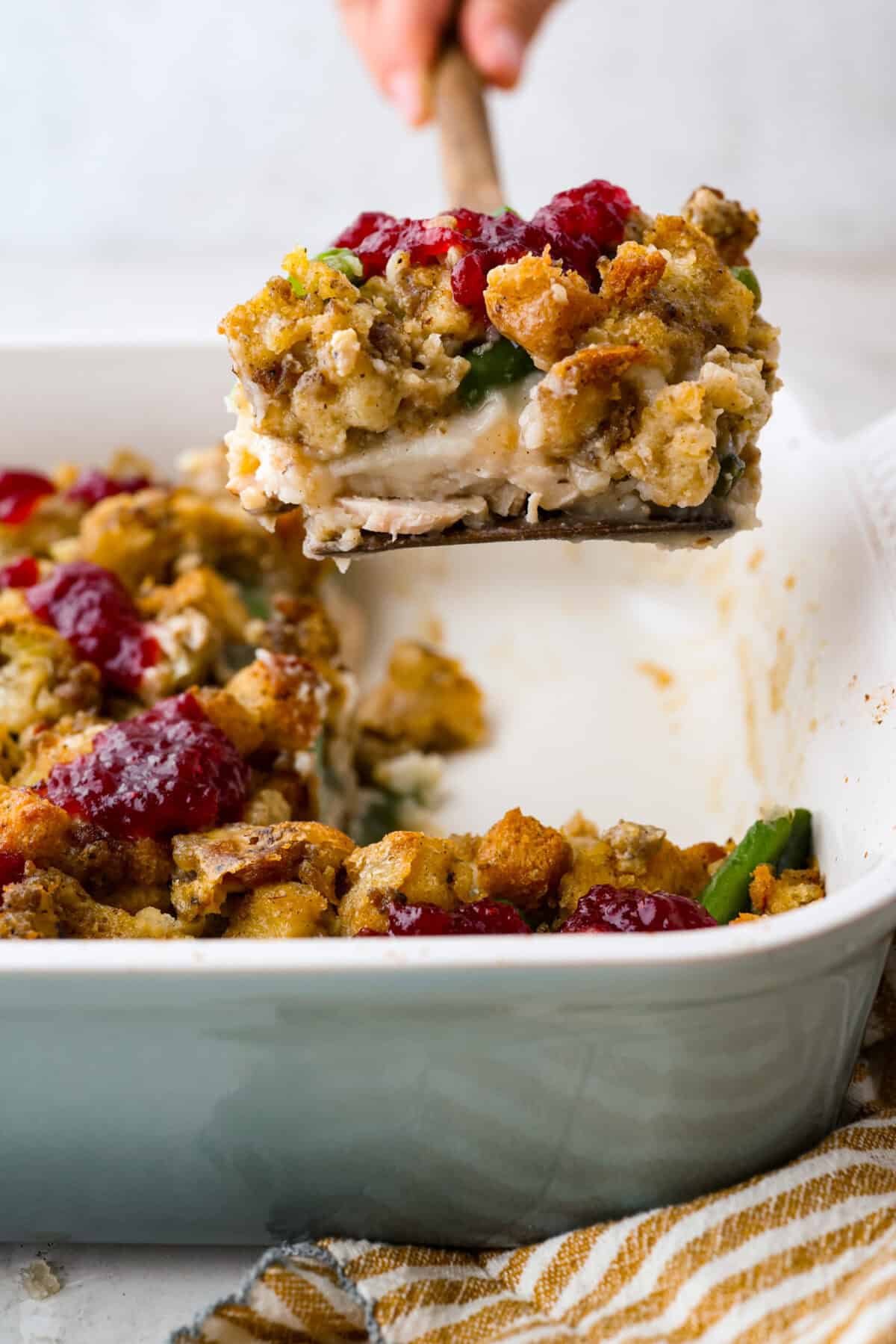 Someone lifting a serving of Thanksgiving leftover casserole out of the baking dish. 