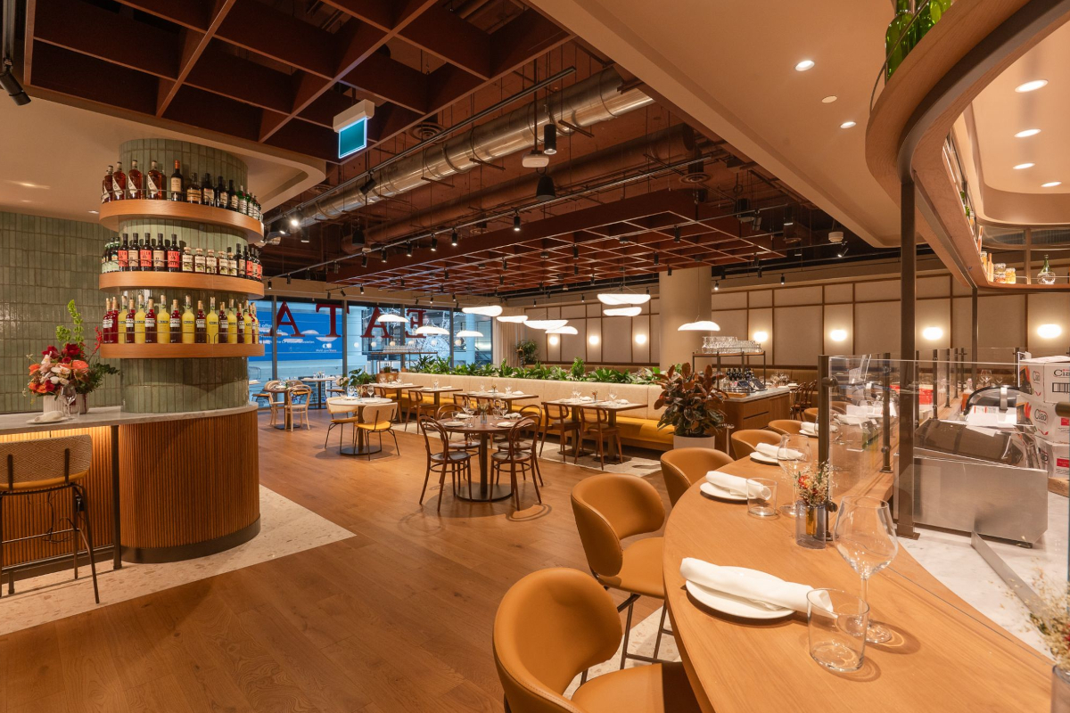 Eataly Toronto restaurant interior. Modern design with wood floors, tables, and bar. Shelves of Italian food products.