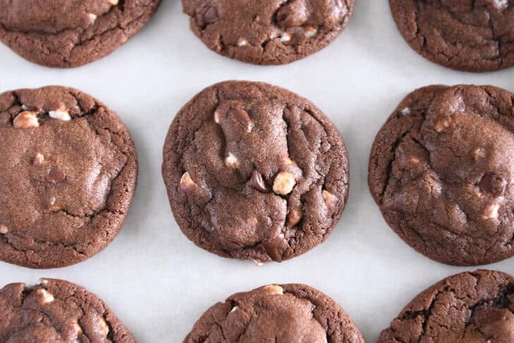 Baked hot cocoa chocolate cookie with mini marshmallow bits on parchment-lined baking tray.