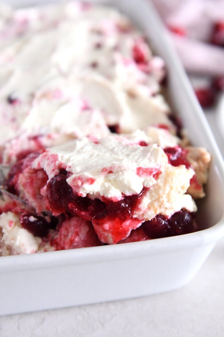 Scoop of cranberry orange angel food cake dessert in white baking pan.