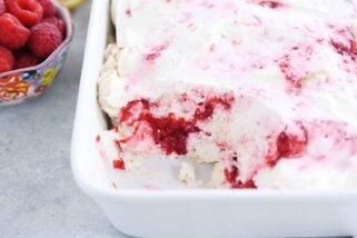 layered angel food cake, raspberries and whipped cream in white baking dish with scoop taken out
