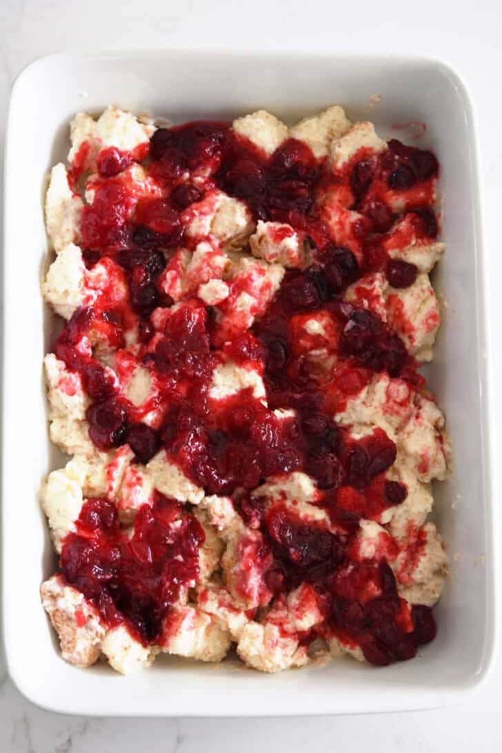 White baking dish with cream-covered angel food cake cubes topped with cranberry orange mixture.