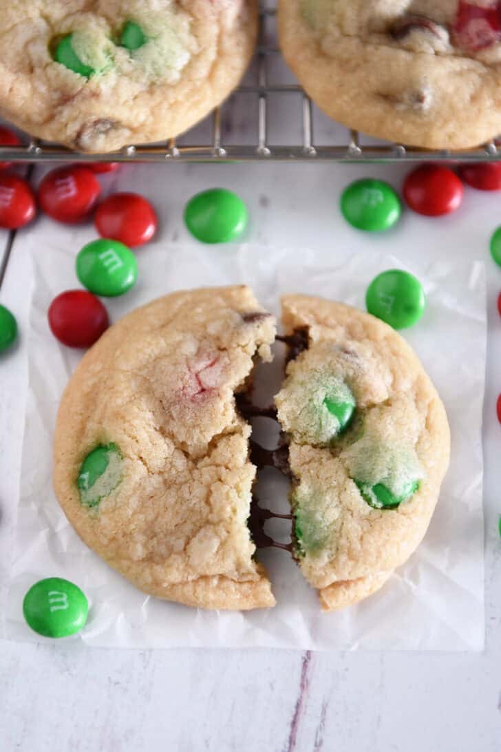 Baked chocolate chip cookie with red and green M&Ms in half with melty chocolate chips.