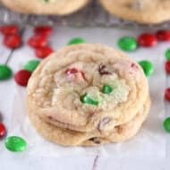 Two baked chocolate chip cookies with red and green M&Ms stacked on parchment paper.