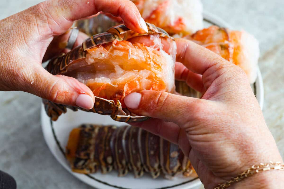 Someone using their hands to lift the lobster tail meat up.