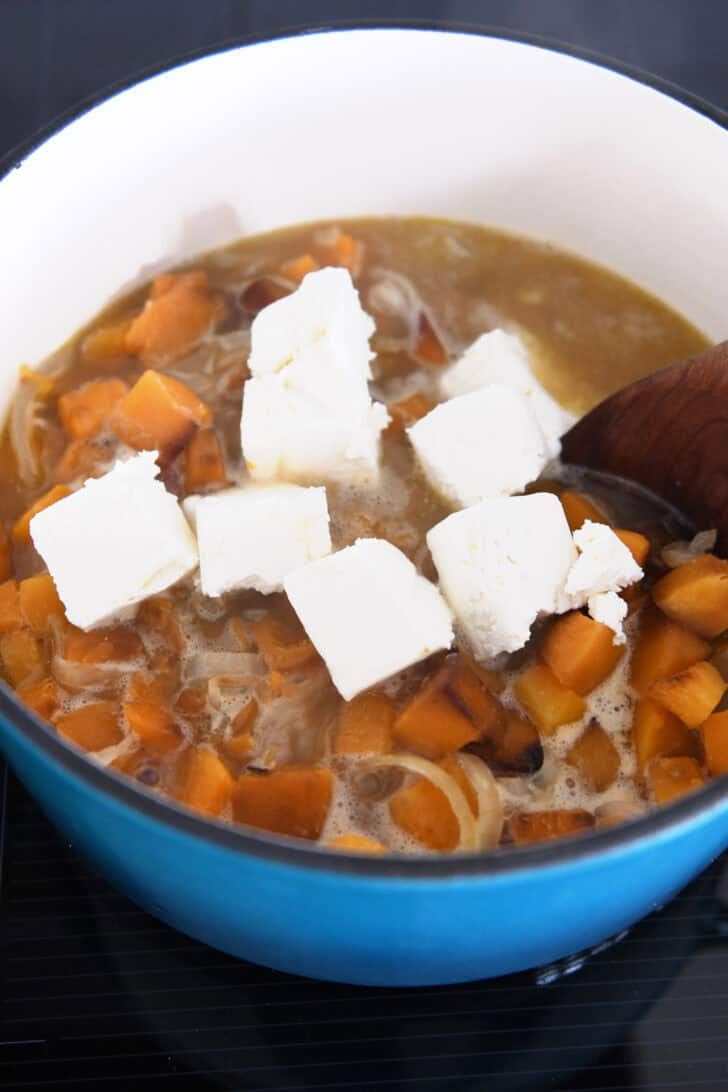 Soup pot with cubed cream cheese, broth, butternut squash pieces and onions.