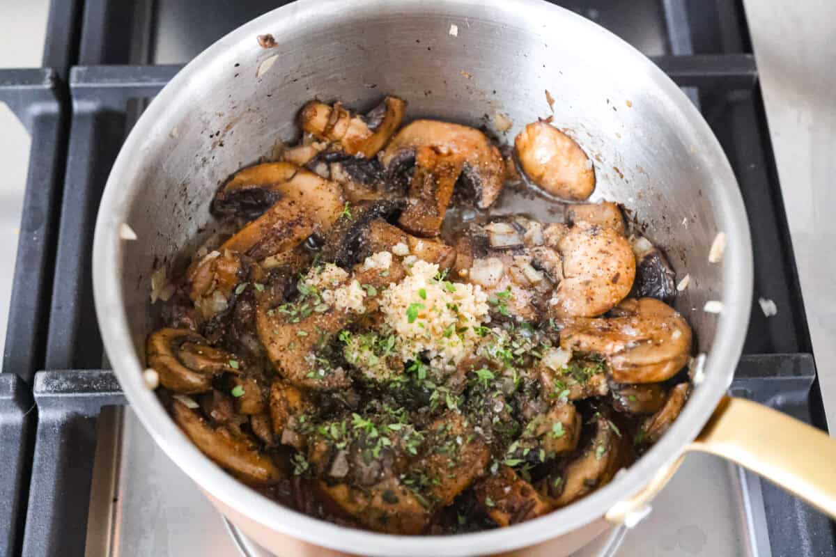 Mushrooms in a pot cooked down with onions and garlic and fresh thyme added to it. 