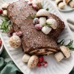 yule log cake on platter decorated with meringue mushrooms and sugared cranberries