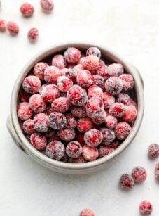 sugared cranberries in white bowl with scattered cranberries surounding bowl