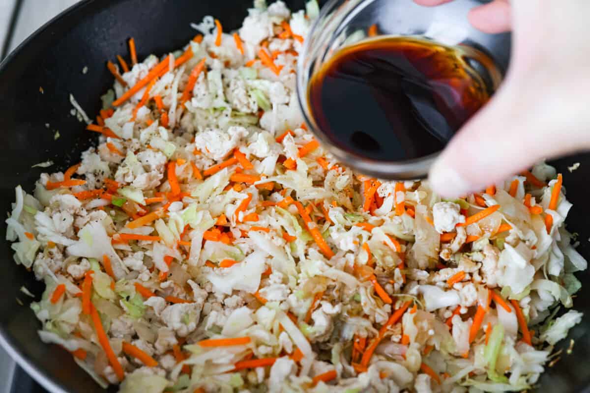 Soy sauce being poured over the coleslaw and turkey mixture. 