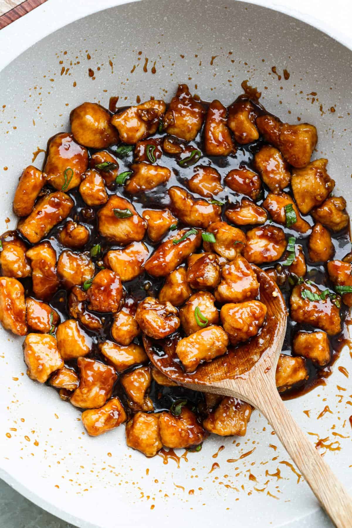 One pan general Tso's chicken in a skillet with a wooden spoon. 