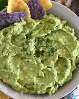 Top down view of homemade guacamole in tan bowl with chopped cilantro and tortilla chips.