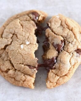 Soft melty brown butter chocolate chip cookie split in half on parchment paper.
