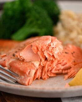 Salmon on gray plate with fork, lemon wedges, cooked broccoli and rice pilaf.