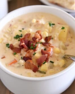 White bowl with spoon scooping up chowder with fresh corn, bacon, potatoes and carrots.