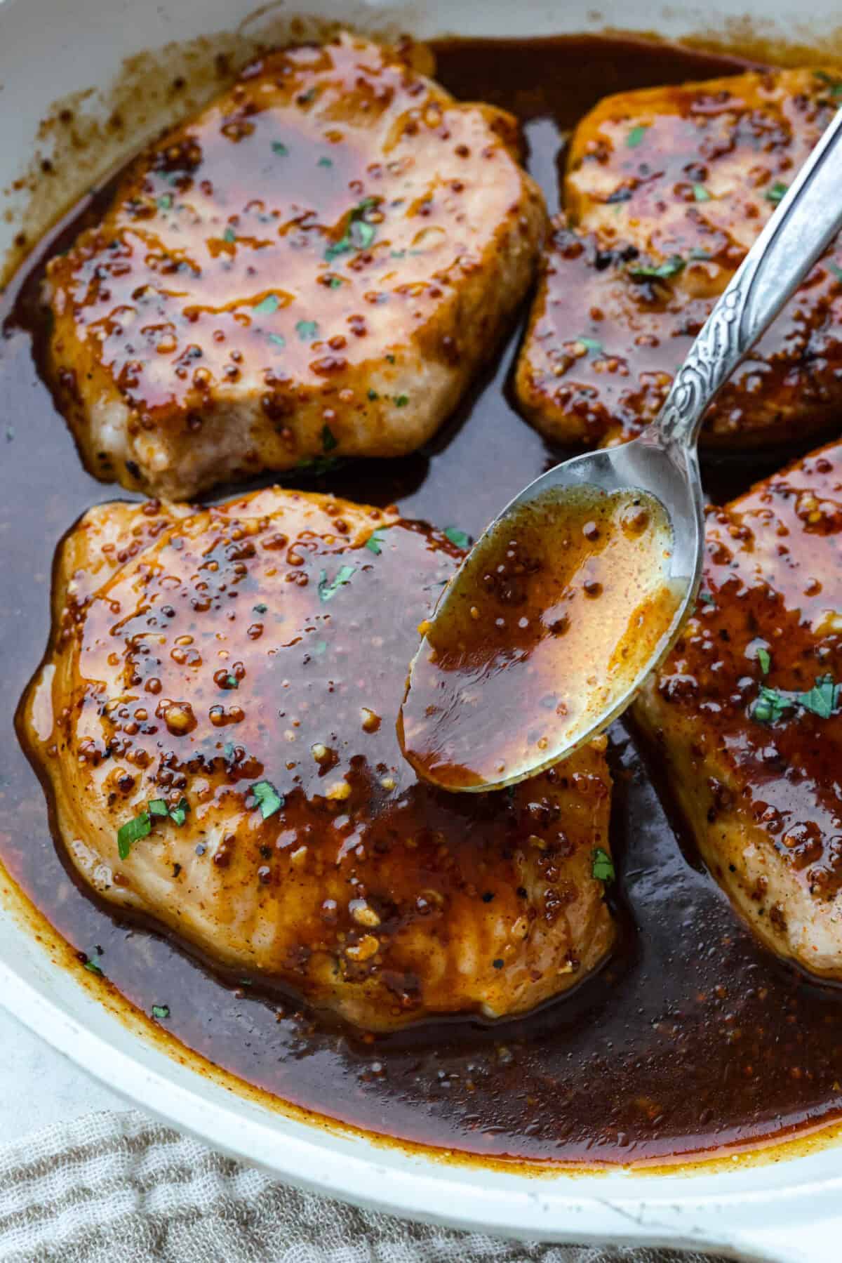 Close up of someone spooning honey mustard sauce over the pork chops.