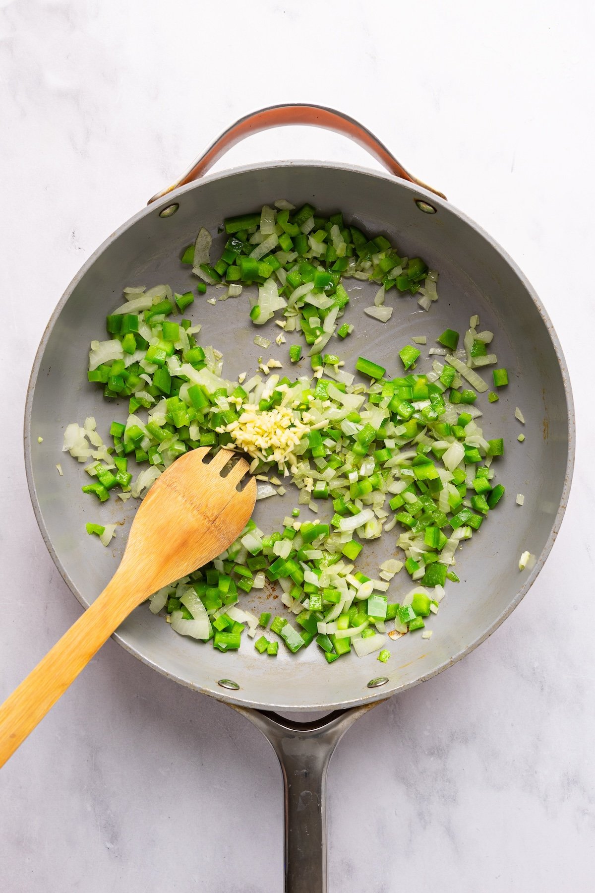large skillet with minced garlic added to onion and green pepper