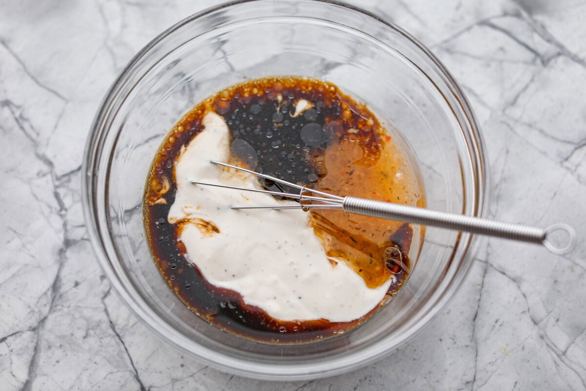 Sauce ingredients added to a mixing bowl with a small whisk.