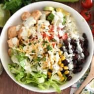 White bowl with cooked chicken, chopped tomatoes, cilantro lime rice, chopped avocados, black beans, roasted corn, and lettuce.