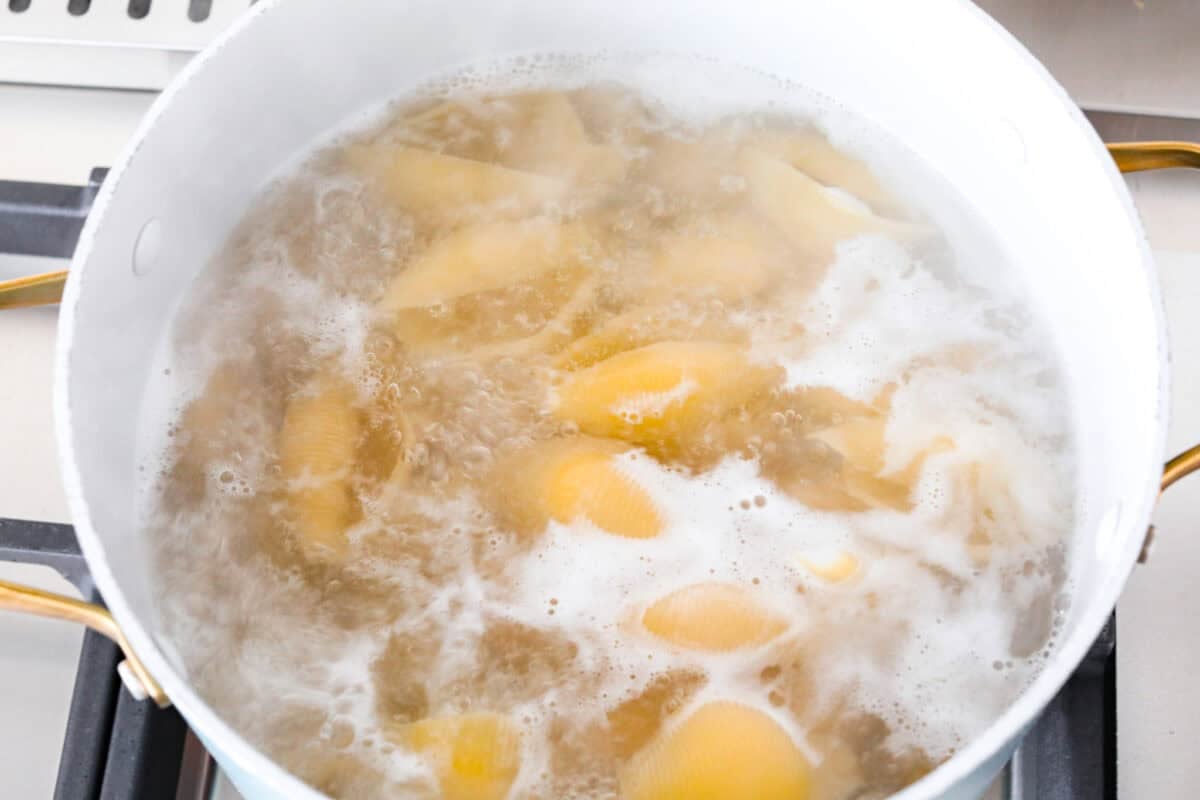 Jumbo shells cooking in boiling water on the stove.