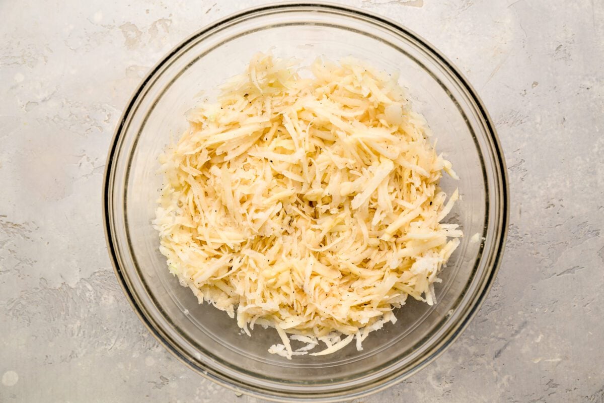 glass bowl with shredded potatoes and onions seasoned with salt and pepper