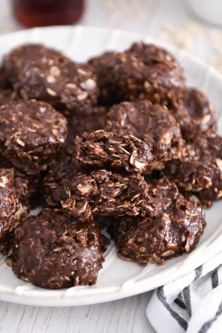 Stack of chocolate no-bake cookies on white plate with one cookie broken in half.