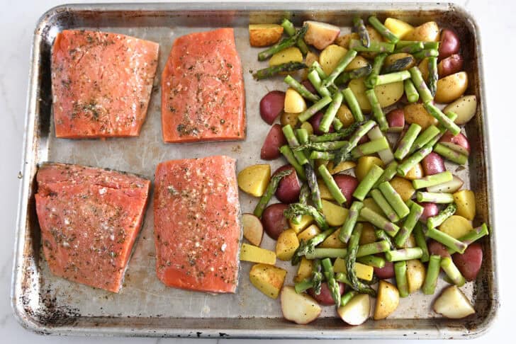 Top down view of sheet pan with asparagus, potatoes, and four filets of salmon.