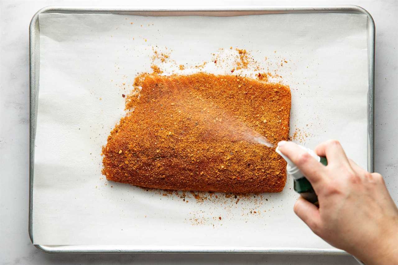 Spraying salmon with oil over a spice rub.