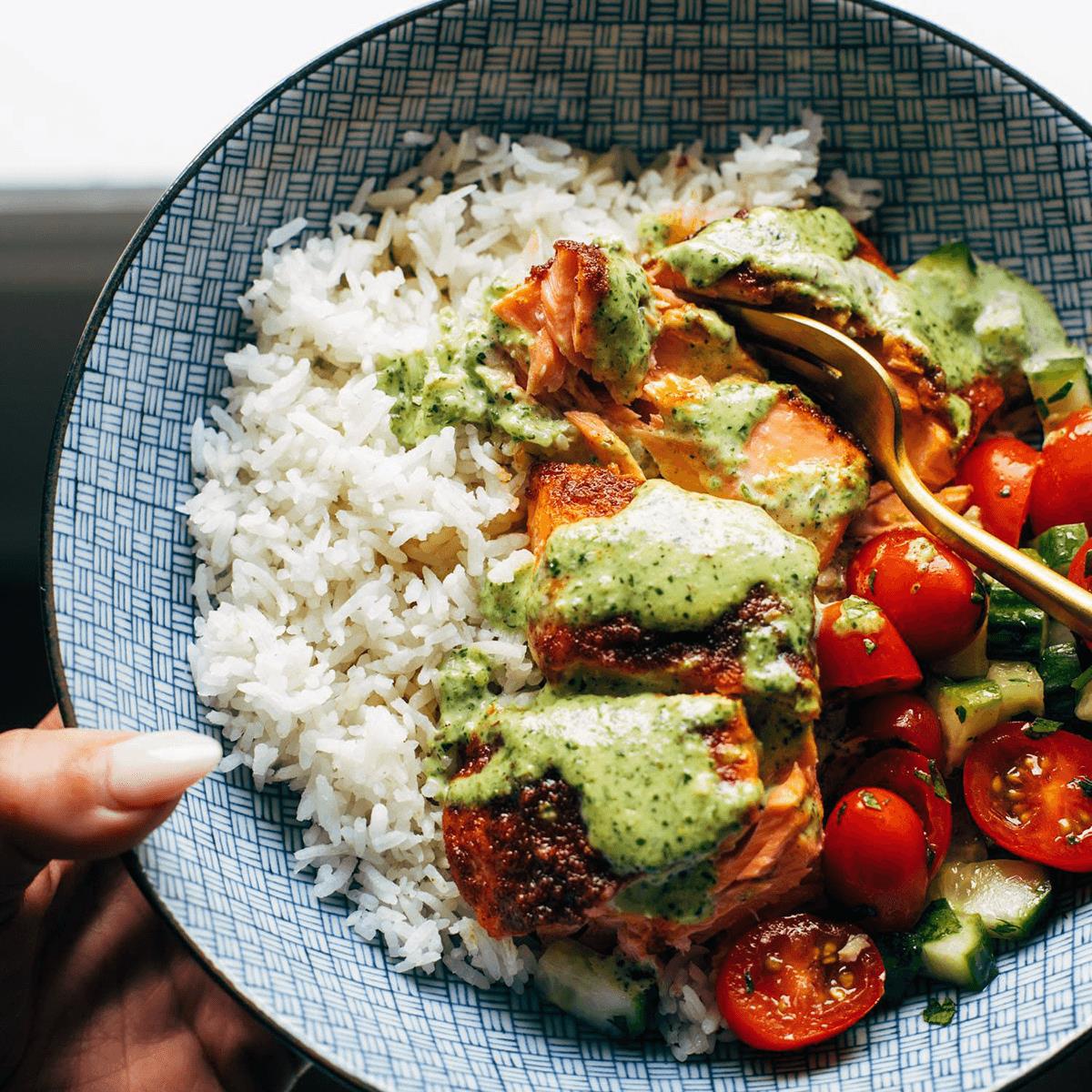 Salmon in a bowl with tomato salad, rice, and basil sauce.
