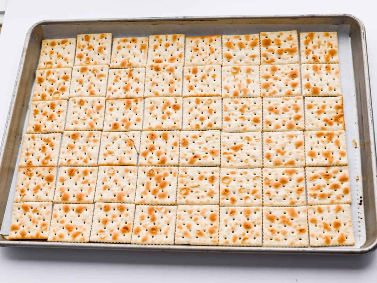 Saltines spread out on a cookie sheet. 