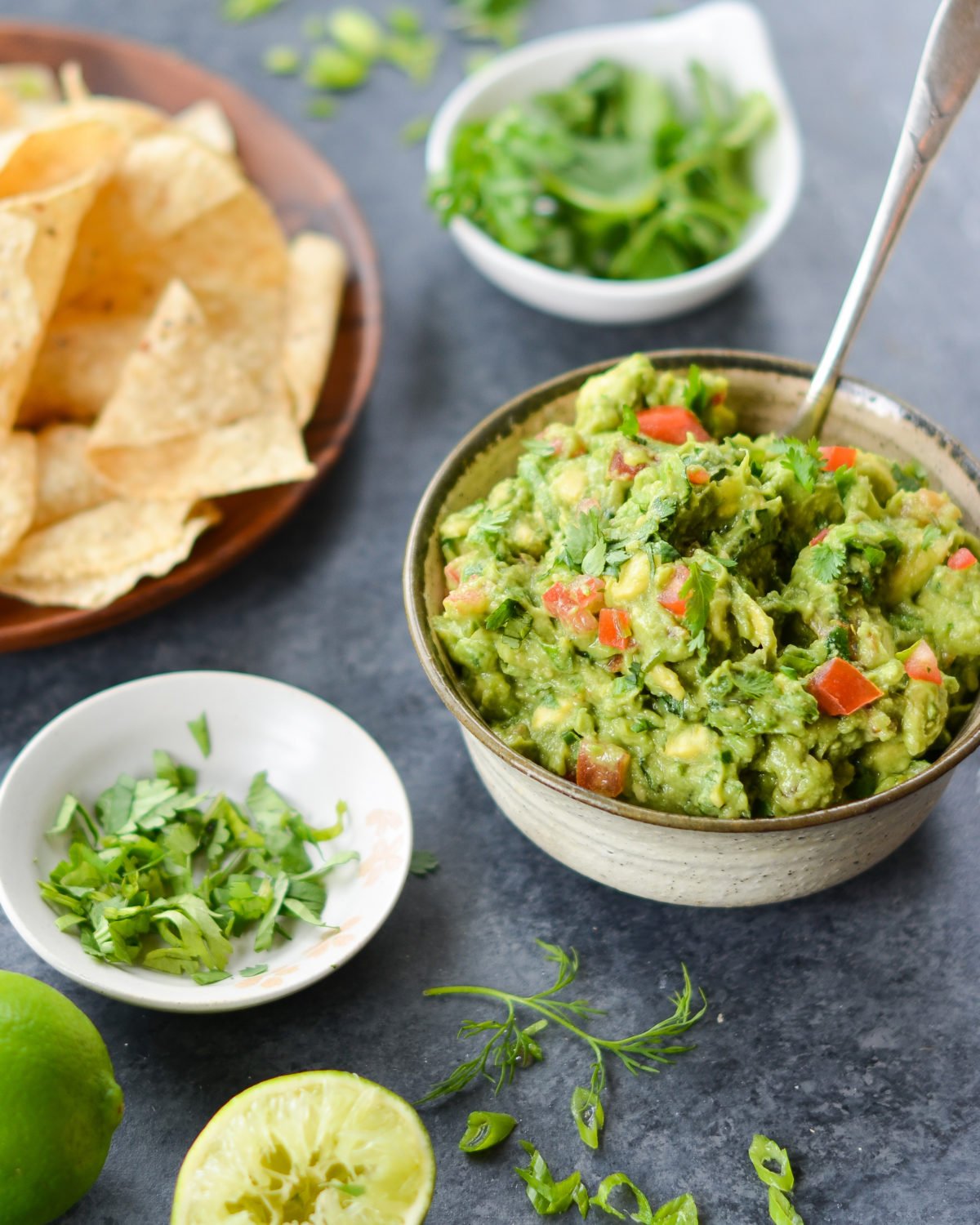 Guacamole in bowl with bowls of cilantro and chips