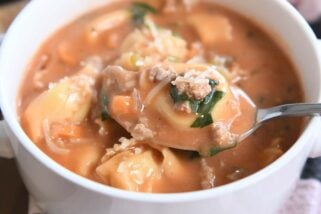 Spoonful of tortellini and creamy tomato broth in white bowl.