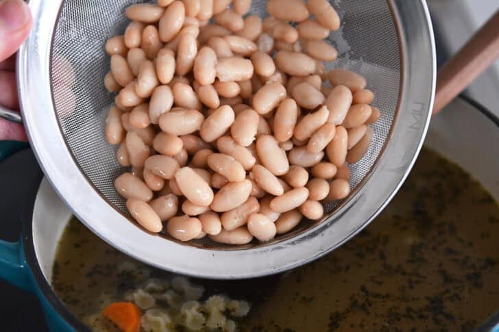 White beans in colander over soup pot.