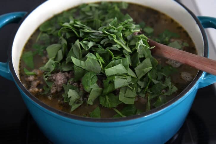 Large pot with fresh, chopped spinach on top of broth and soup.