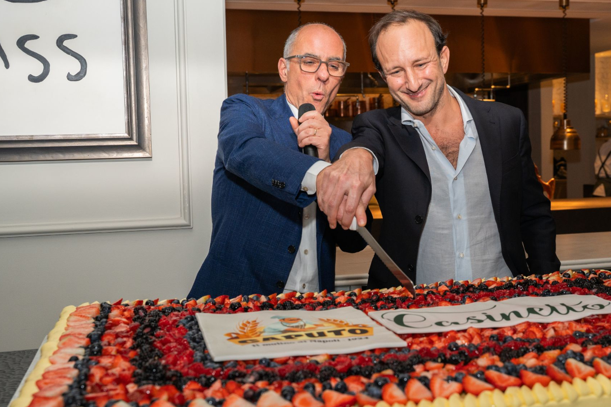 Italian culinary heritage-Two men cut a Caputo and Casinetto cake. The cake is decorated with strawberries and blueberries.