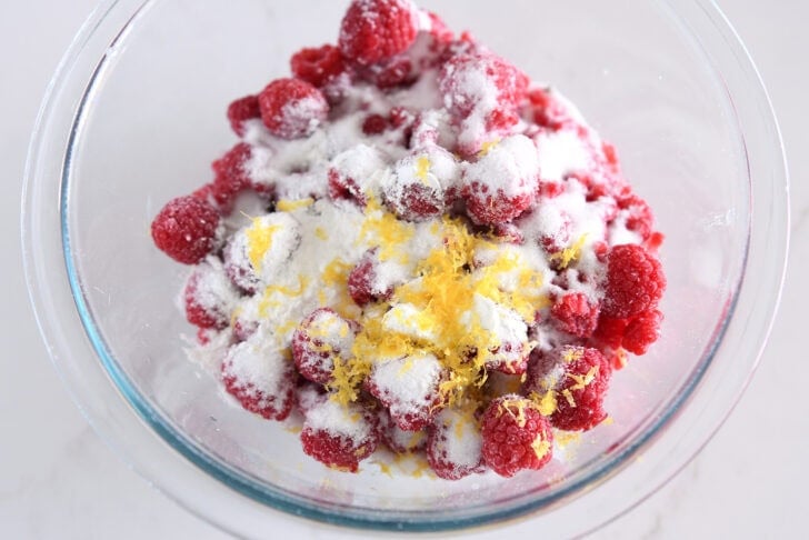 Glass bowl with frozen raspberries, sugar, and lemon zest.