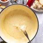 pot of cheese fondue with apple slices, bread cubes, and veggies for dipping
