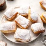sugar-dusted beignets on round white plate with 2 cups of coffee
