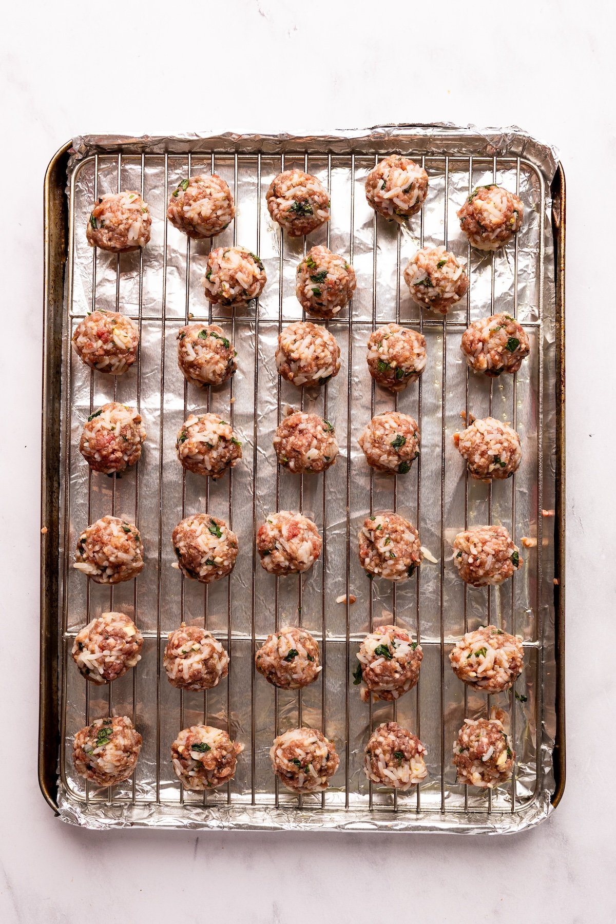 unbaked meatballs arranged on rack on top of foil-lined baking sheet