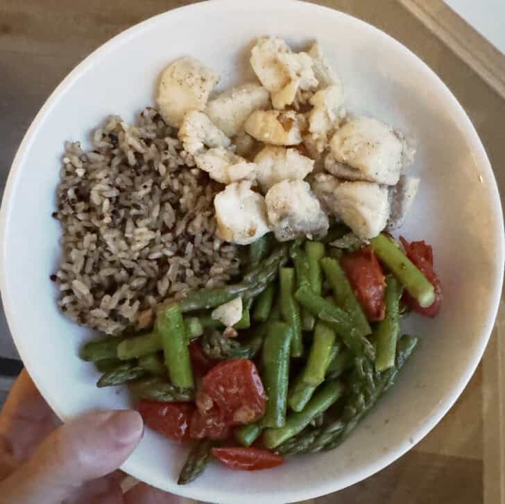 White bowl with brown rice, cod, tomatoes, and asparagus.