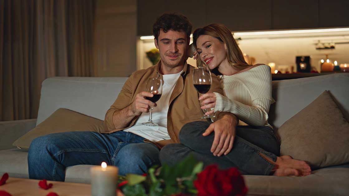 Relaxed couple on couch with wine, candles lit, no stress visible, pure connection