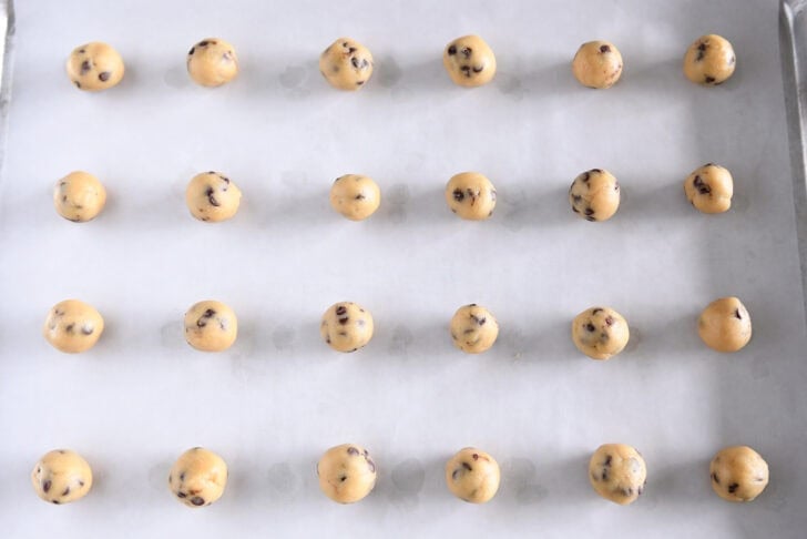 Parchment lined baking tray with 24 unbaked mini cookie dough balls.