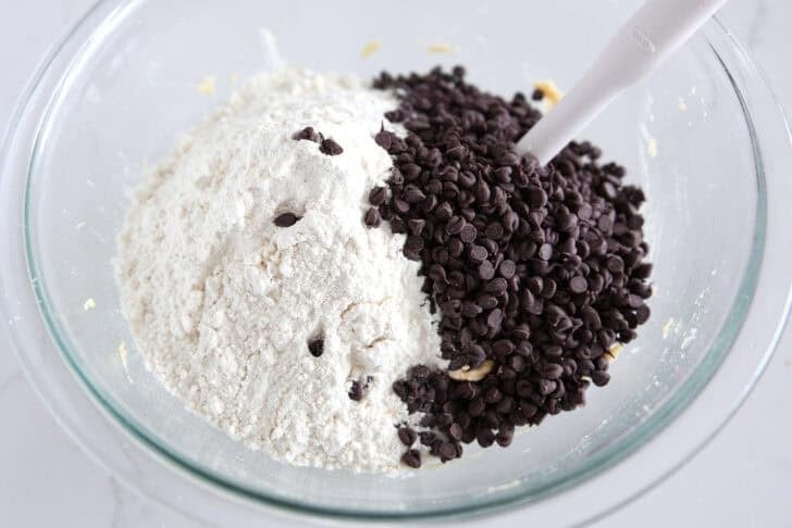 Glass bowl with cookie dough, white flour and mini chocolate chips.