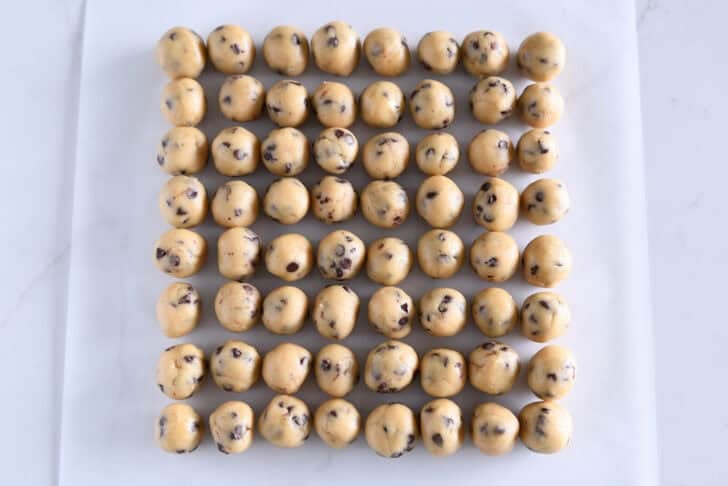 64 mini chocolate chip cookie dough balls on white parchment paper.