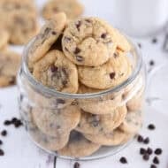 Glass jar filled with mini chocolate chip cookies with mini chocolate chips around bottom.
